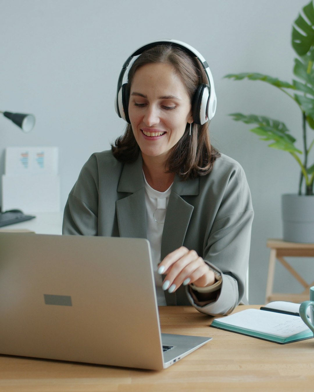 A smiling learner wearing headphones practises a speaking answer at her laptop